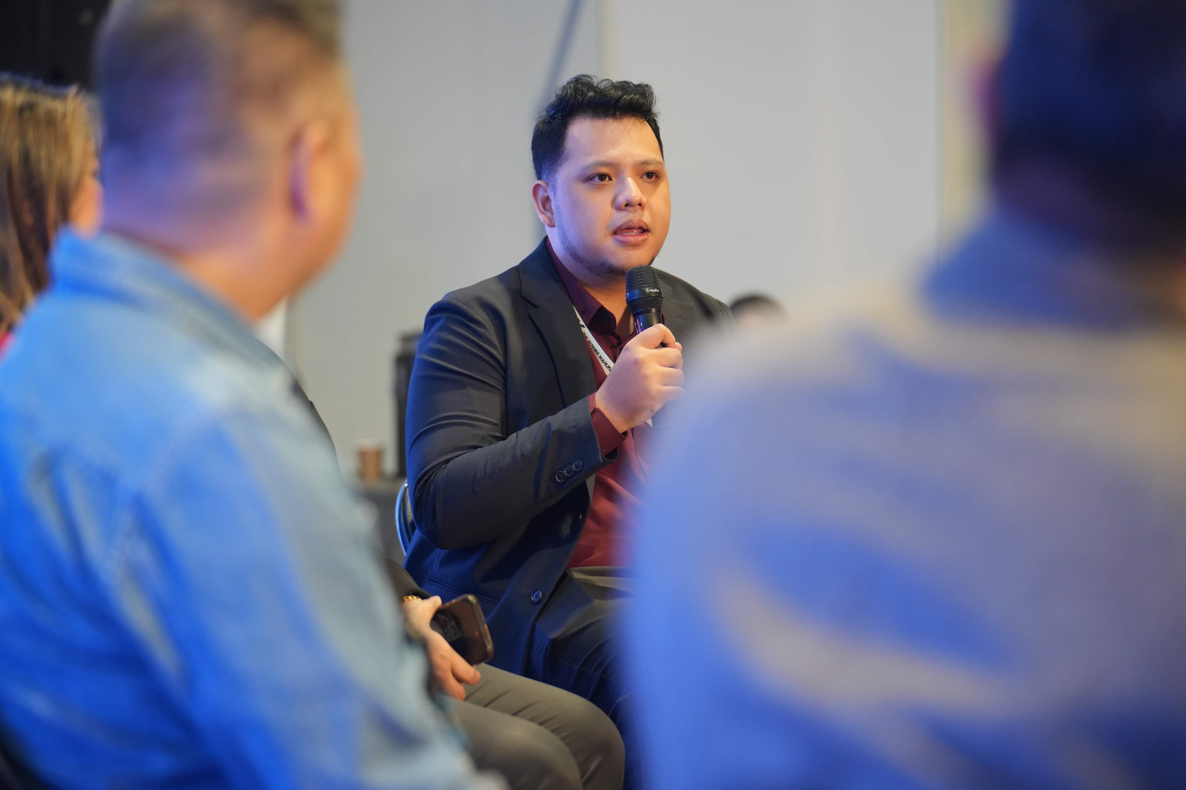Close-up of JC mid-speech during a fireside chat, holding microphone with expressive hand gesture