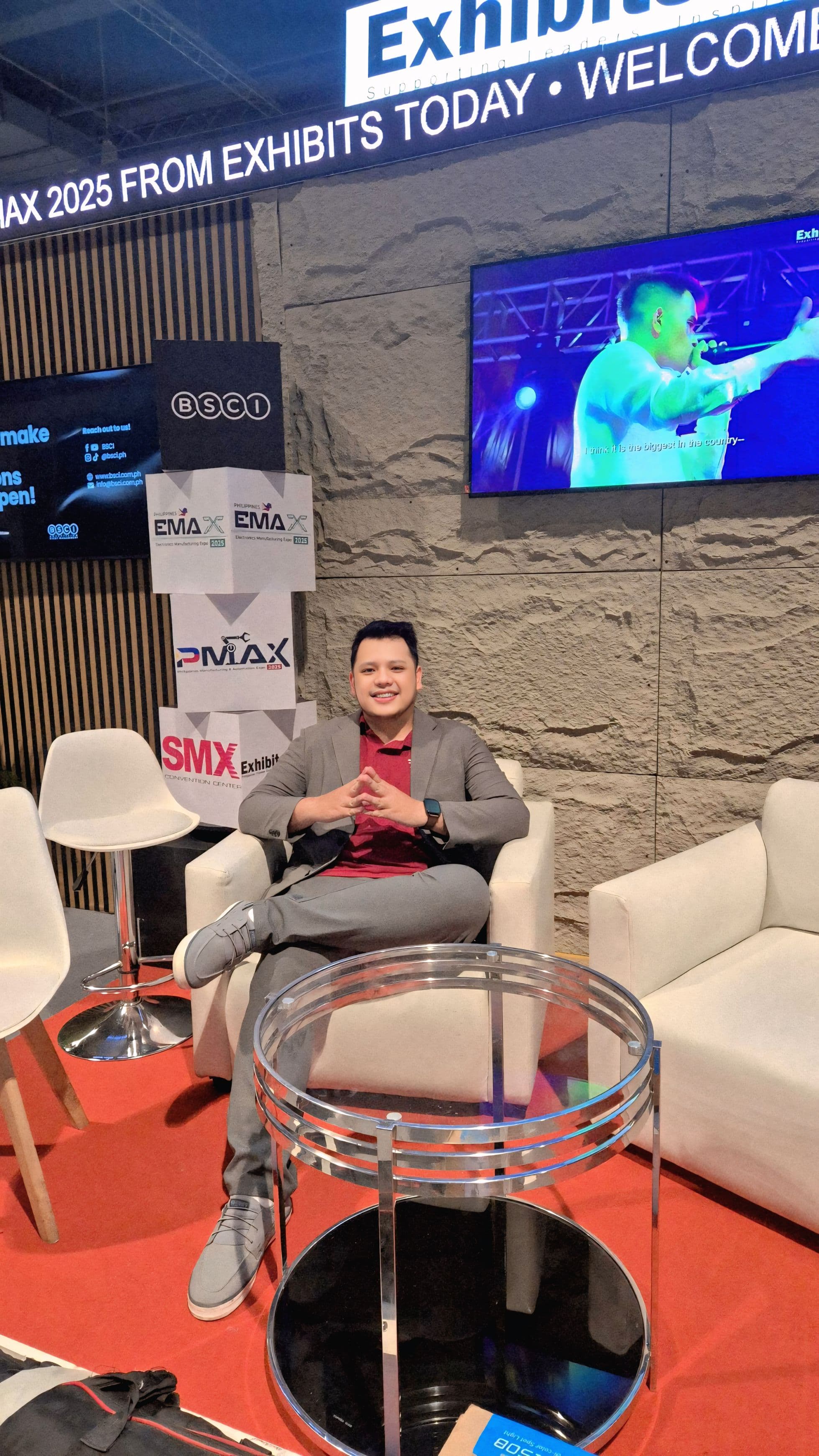 Portrait of JC seated in modern white armchair at PMAX 2025 exhibit booth